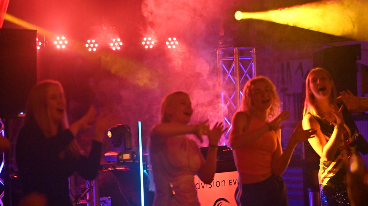 Bezoekers dansen onder rode en gele podiumverlichting bij een dj-show.